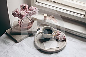 Spring still life composition. Greeting card mockup, marble tray, cup of coffee, old books. Vintage feminine styled