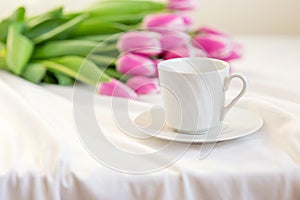 Spring still life with a white mug with a saucer and a bouquet of beautiful pink tulips