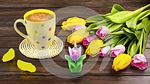 Spring still life with a white polka dot cup of coffee, a bouquet of yellow and pink tulip flowers and a candl