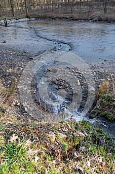 Spring stream flowing from drained muddy pond