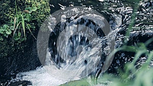 Spring stream flows down rocks and forms foam.