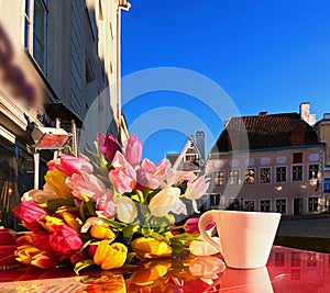 Spring street cafe in Tallinn town square ,cup of coffee on table top and flowers tulip sunlight reflection holiday travel to Esto