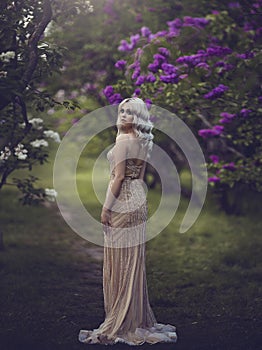 Spring style. Beautiful sensual girl blonde in spring. Blossoming spring garden. Young girl in a gold elegant dress