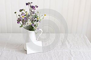 Spring, summer still life. Enamel jug with wild flowers bouquet on linen table cloth. Daisies, bluebells, aquilegia and