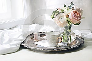 Spring, summer still life scene. Cup of coffee, blank greeting card, envelope on old silver tray at windowsill. Vintage