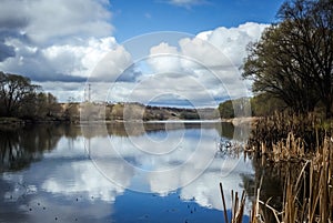 Spring Sunny landscape, white clouds and blue sky are reflected in the river water.