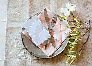 Spring Table Place Setting with white flowers, pink napkin, silverware and a blank card for party menu or invitation.