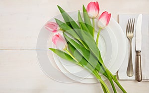 Spring table setting with pink tulips on white wooden background. Top view, copy space