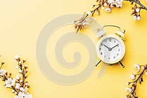 Spring time background. May flowers and April floral nature with alarm clock on yellow. Branches of blossoming apricot