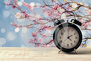 Spring time change concept with alarm clock on wooden table over nature tree blossom