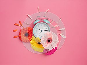 Spring time concept. Creative flat design with turquoise alarm clock on pink background with vibrant colorful flowers around it