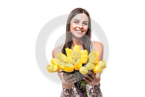 Spring time. Young portrait of woman with flowers yellow tulips in hands on a light background