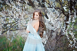 Spring touch. Happy beautiful young woman in blue dress enjoy fresh flowers and sun light in blossom park at sunset