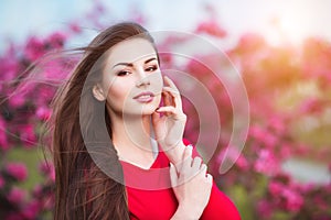 Spring touch. Happy beautiful young woman in red dress enjoy fresh pink flowers and sun light in blossom park at sunset.