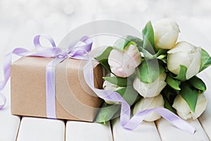 Spring tulip flowers and gift box with bow ribbon on white table. Greeting card for Birthday, Womens or Mothers Day.