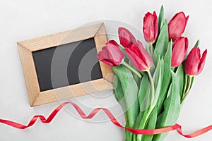 Spring tulip flowers with ribbon and wooden frame with empty space for text on gray stone table top view in flat lay style.