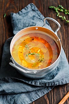 Spring vegetable soup with chicken stock in a pot on kitchen wooden table.