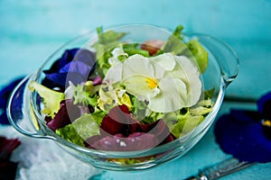 Spring vitamin salad: greens with cherry tomatoes and edible flowers (pansies) on a blue wooden background. The concept of healthy