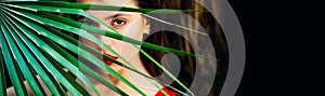 Spring woman face for banner. Sexy beautiful woman hiding behind the palm leaves. Sensual model girl with smooth skin