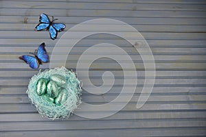 Springtime Easter decoration with blue nest filled with shiny chocolate eggs and butterfly shape decorations
