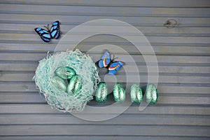 Springtime Easter decoration with blue nest filled with shiny chocolate eggs and butterfly shape decorations