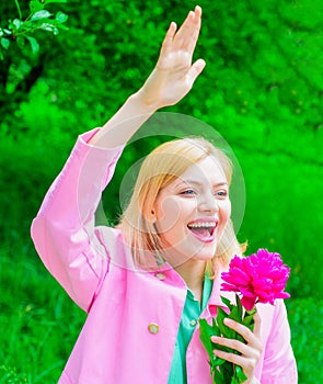 Springtime. Happy woman with peony flower waving hand. Smiling girl welcoming to friends.