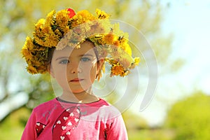 Springtime portrait of a cute two years old girl posing with a dandelion wreath