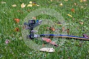 Sprinkler in grass with fallen leaves and hose