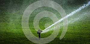 Sprinkler in Park Spraying Water on Lush Green Grass