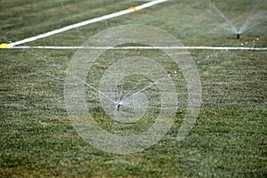 Sprinklers Automatic lawn grass irrigation system in stadium. Football, soccer field in small provincial town. Underground