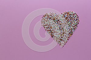 Sprinkles arranged in a heart shape on a pink rustic background. Valentine's Day, greeting card. Sprinklers for photo