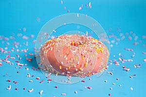 Sprinkles falling from top on Tasty pink strawberry donut. Delicious dessert on blue background.