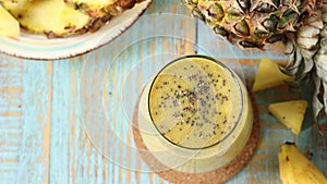 Sprinkling chia seeds on yellow pineapple banana tropical smoothie placed on wooden table
