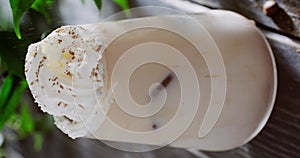 Sprinkling cinnamon powder on Iced coffee latte cocktail in glass, cocktail with coffee ice cubes, whipped cream on top