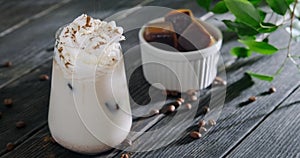 Sprinkling iced coffee drink with cinnamon, latte with milk froth, cream topping and ice cubes, glass placed on wooden