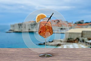 Spritz cocktail on a table with view of Dubrovnik fortress walls, beach