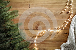 Spruce twigs and warm scarf and lights on wooden table flat background. Christmas decorations on wooden board top seen from above.