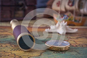 Spyglass, a brass compass and a starfish lie on an old map against the background of a wooden model of a sailboat.