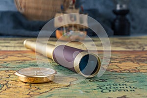Spyglass and a compass lie on an old map against the background of a model of a wooden sailboat.