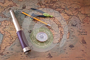 Spyglass, compass and a pencil with a measuring instrument lie on an old map.