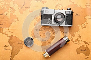Spyglass, photo camera and compass on vintage world map. Travel planning concept