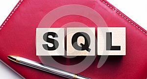 SQL is made up of wooden cubes that stand on a burgundy notebook near the pen. Business concept