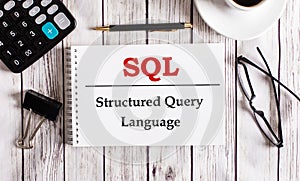 SQL Structured Query Language is written in a white notepad near a calculator, coffee, glasses and a pen. Business concept