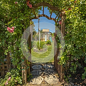 Square Arched wooden arbor at the entrance of a garden with playhouse slides and swings