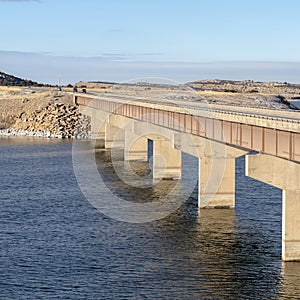 Square Beam bridge with deck supported by abutments or piers spanning over blue lake