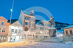 Square in bergen ar night, statue and houses covered in snow and ice. Colorful houses aroud lit by streetlamps and snow capped