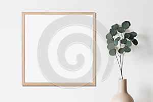 Square blank frame mockup in minimal interior design with trendy plant in vase on empty white wall background. Minimalism concept