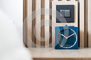 Square blue analog alarm clock on table in bedroom. Minimal clock style