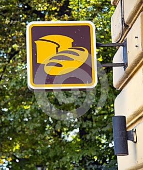 A square sign with bread painted on it hangs on the corner of the building