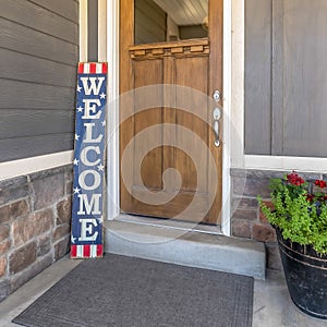 Square Brown front door with glass pane and Welcome sign against gray and stone wall